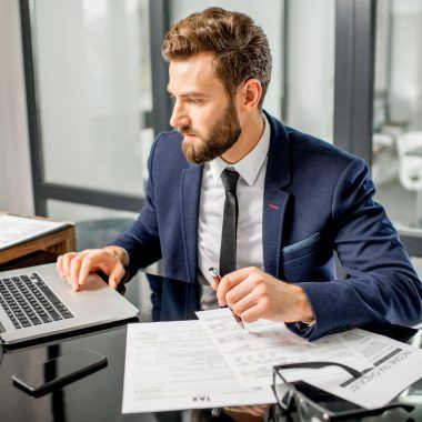 An accountant looking at a laptop, holding documents.